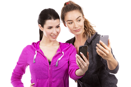 young casual caucasian women wearing sport outfits on white isolated background. Holding mobile phones.の写真素材