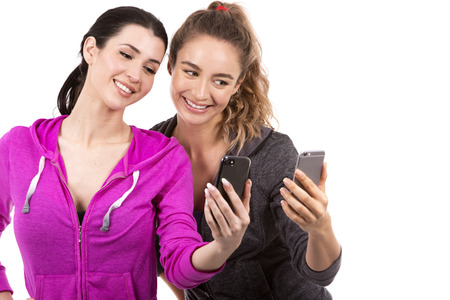 young casual caucasian women wearing sport outfits on white isolated background. Holding mobile phones.の写真素材