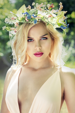 beautiful woman with pretty makeup and pink lipstick posing outdoors wearing spring and summer dress and flower crownの写真素材