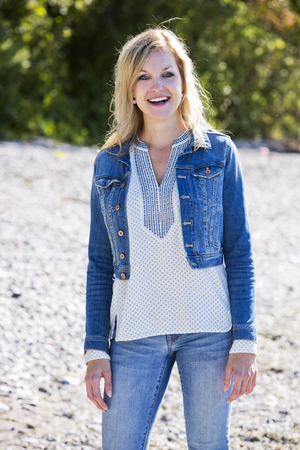 young blonde woman is wearing jeans, posing outdoors on the beachの写真素材