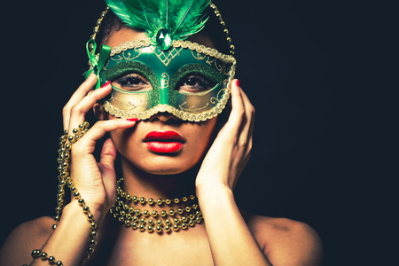 Upscale Indian woman wearing gold jewellery and red lipstick on black background. Green party mask.の写真素材