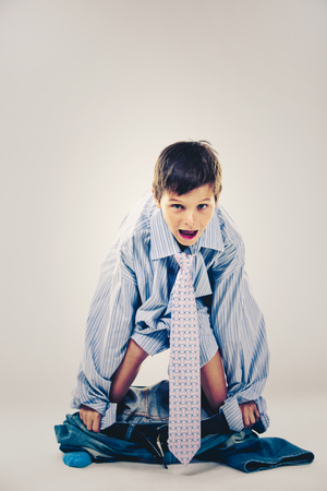 Caucasian boy wearing his Dad's shirt, jeans and tie on light background. He is wearing big adult size clothes which are too big for him.の写真素材