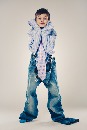 Caucasian boy wearing his Dad's shirt, jeans and tie on light background. He is wearing big adult size clothes which are too big for him.の写真素材