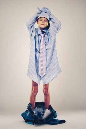Caucasian boy wearing his Dad's shirt, jeans and tie on light background. He is wearing big adult size clothes which are too big for him.の写真素材