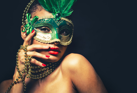 Upscale Indian woman wearing gold jewellery and red lipstick on black background. Green party mask.の写真素材