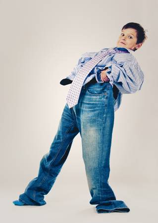 Caucasian boy wearing his Dad's shirt, jeans and tie on light background. He is wearing big adult size clothes which are too big for him.の写真素材