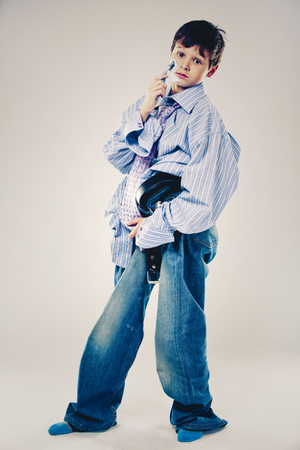 Caucasian boy wearing his Dad's shirt, jeans and tie on light background. He is wearing big adult size clothes which are too big for him.の写真素材