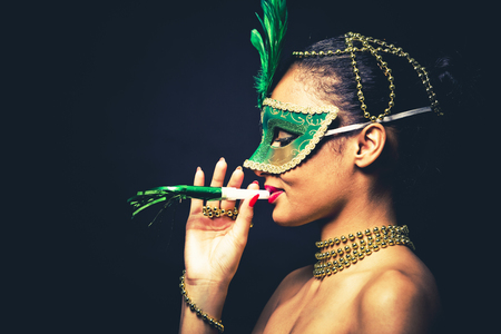 Upscale Indian woman wearing gold jewellery and red lipstick on black background. Green party mask.の写真素材