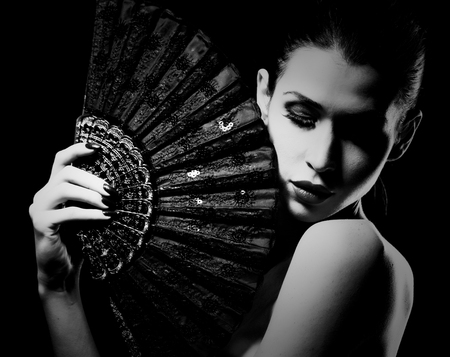 beautiful caucasian brunette holding a fan. Hiding and being mysterious on black background. Black and white photo.の写真素材