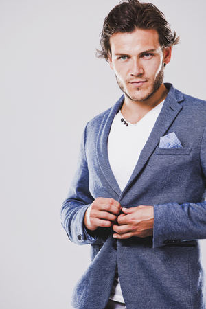 Fashion portrait of a handsome man with trendy hairstyle in a stylish jacket on light backgroundの写真素材
