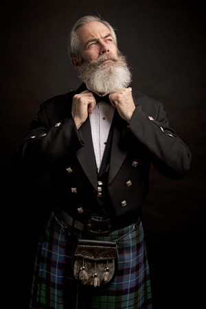 Close up of senior man with grey hair and full beard, wearing scotting kilt on dark backgroundの写真素材