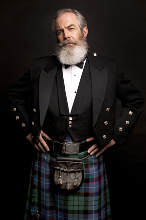 Close up of senior man with grey hair and full beard, wearing scotting kilt on dark backgroundの写真素材