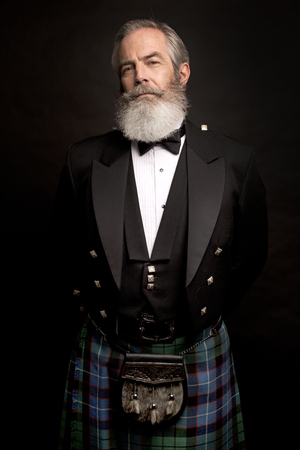 Close up of senior man with grey hair and full beard, wearing scotting kilt on dark backgroundの写真素材