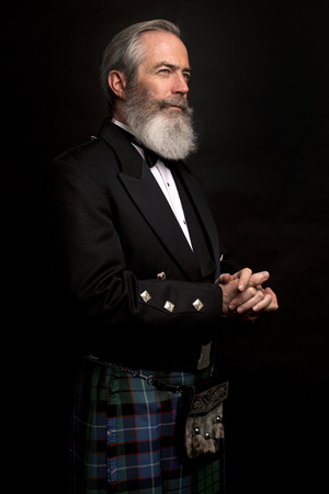 Close up of senior man with grey hair and full beard, wearing scotting kilt on dark backgroundの写真素材
