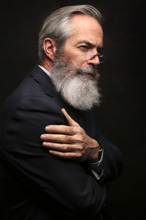 Close up of senior man with grey hair and full beard, wearing suit on dark backgroundの写真素材