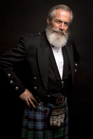 Close up of senior man with grey hair and full beard, wearing scotting kilt on dark backgroundの写真素材