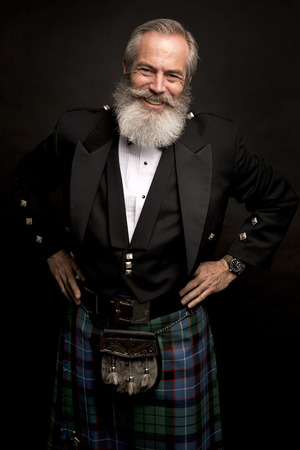 Close up of senior man with grey hair and full beard, wearing scotting kilt on dark backgroundの写真素材