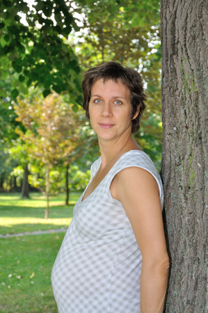 Pregnant woman leaning on the tree in the city parkの写真素材