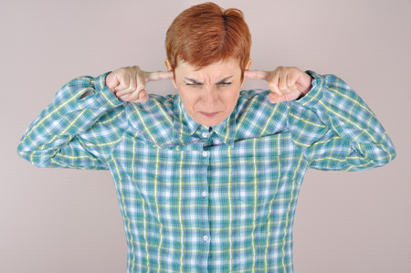 Frowning woman bending her head and holding her index fingers in the ears because of loud noiseの写真素材