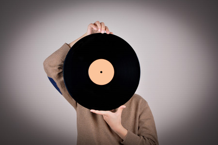 Young boy wearing a brown sweater covering his face with the vinyl record. Isolated on gray background and added vignette. Vintage style photoの写真素材