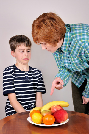 Strict woman showing a cute young boy fruit he has to eatの写真素材
