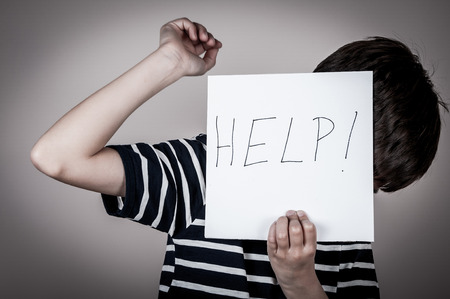 Scared and abused young boy holding the paper with handwritten help sign. Low keyの写真素材
