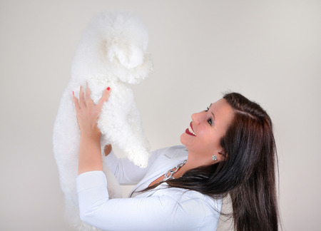Smiling glamorous woman in white holding white fluffy dog isolated on gray backgroundの写真素材