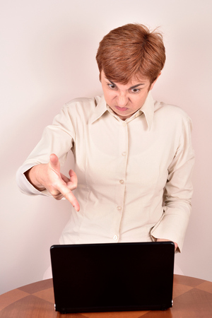 Angry businesswoman making a grimace and pretending to be shooting at the laptop with her handの写真素材