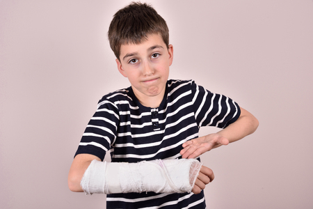 Young boy making a grimace and showing his broken arm with plasterの写真素材