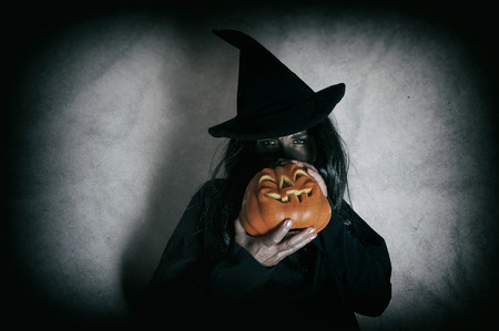 Witch holding halloween pumpkin. Low key. Computer added dirt, scratches, grain and vignette.の写真素材