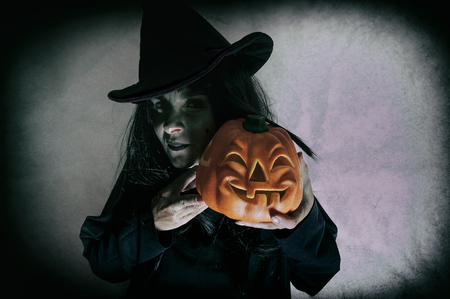 Witch holding halloween pumpkin. Low key. Computer added dirt, scratches, grain and vignette.の写真素材