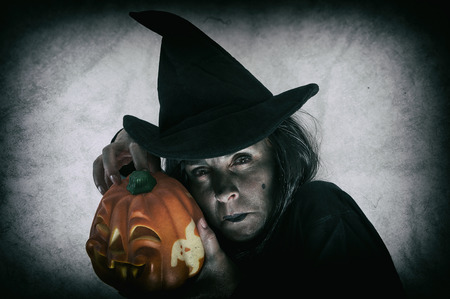 Witch holding halloween pumpkin. Low key. Computer added dirt, scratches, grain and vignette.