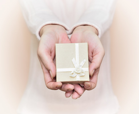 Hands of a woman showing a gift: little beige box with a ribbon. Selective focus.の写真素材