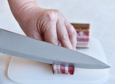 Hands of a woman cutting bacon in small pieces. Selective focus.の写真素材