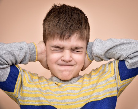 Young boy with closed eyes covering ears with hands