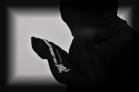 Female robber with black tights over her head holding and looking at the stolen jewellery. Black and white. Low key. Selective focus.の写真素材