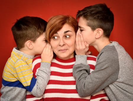 Sons whispering secret into ears of surprised motherの写真素材