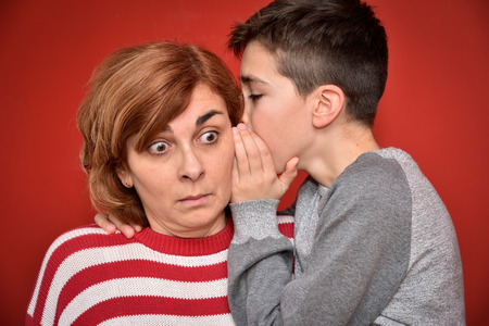Young boy whispering secret into ears of surprised mother