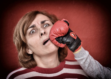 Woman being punched with red boxing glove in her face. Computer added  dust, scratches, grain and vignette.の写真素材
