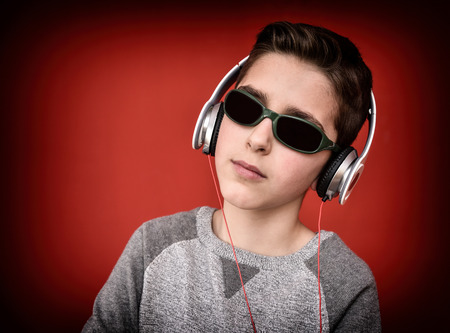 Young boy with headphones and sunglasses listening to music and enjoying. Isolated on the red backgroundの写真素材