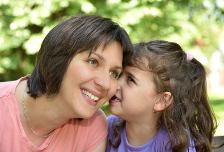 Daughter whispering secret into ears of smiling motherの写真素材