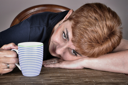 Tired woman with freckles and short hair holding a cup of coffee. Selective focus.の写真素材
