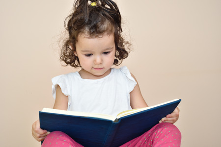Talented cute three-year-old girl reading a book. Selective focus.