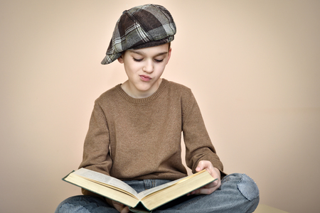 Young boy with cap sitting, holding an old book on the lap and reading. Vintage style.の写真素材