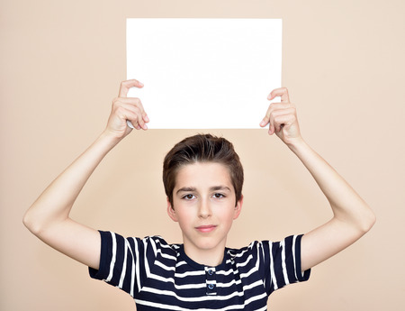 Young boy holding a blank white paper above his headの写真素材