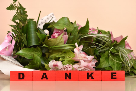 Bouquet of flowers and red wooden blocks with Danke message. Selective focus.