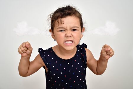 Angry and aggressive young girl with clenched teeth and fists and steam blowing out of her ears looking at the cameraの写真素材