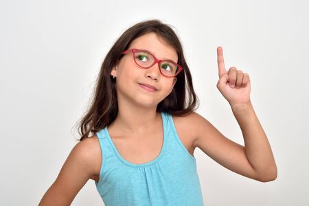 Thoughtful smiling young girl wearing glasses with index finger up having a good idea. She is  looking up.の写真素材