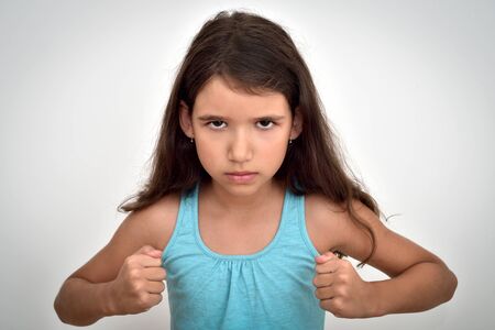Angry and aggressive young girl with clenched fists looking at the camera. Childhood and expressions...