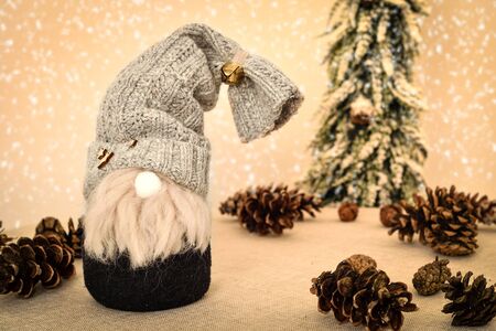 Decorated handmade gnome with pine cones on the table in front of the Christmas tree and snowy...